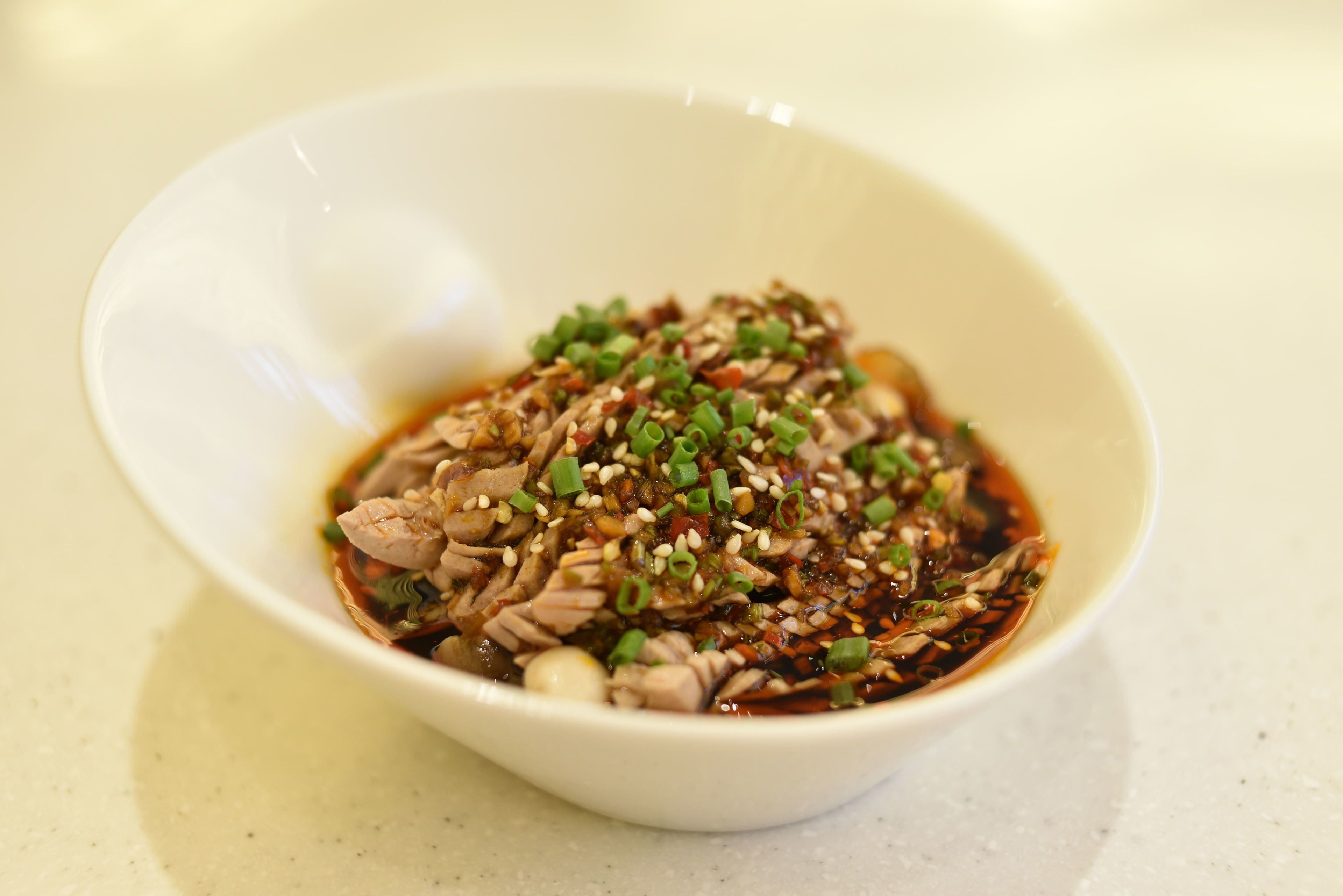 A white bowl containing a dish with shredded meat, green onions, and sesame seeds.