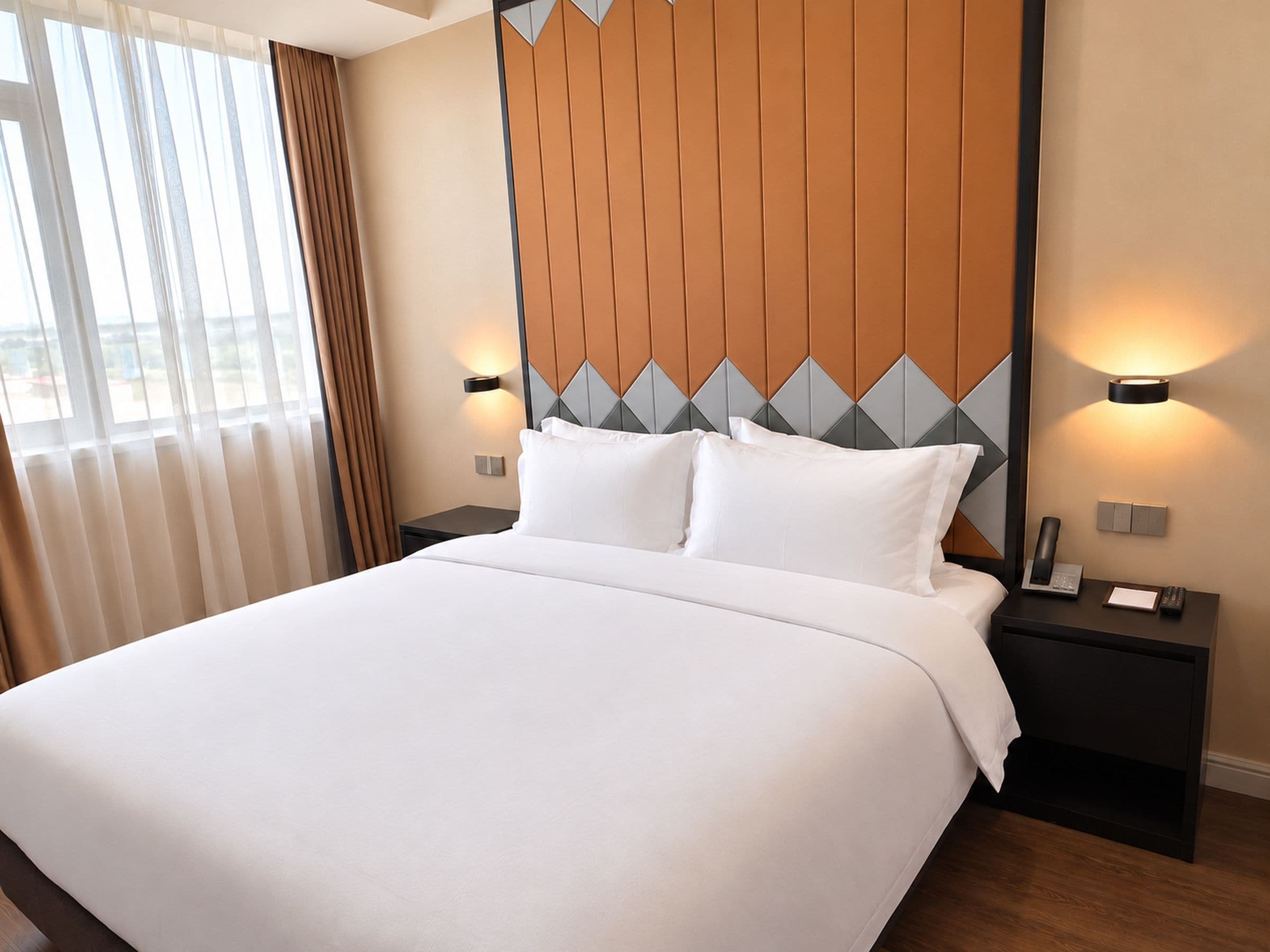Una habitación de hotel con una cama grande, dos mesitas de noche, un cabecero con diseños geométricos y vistas a través de la ventana.