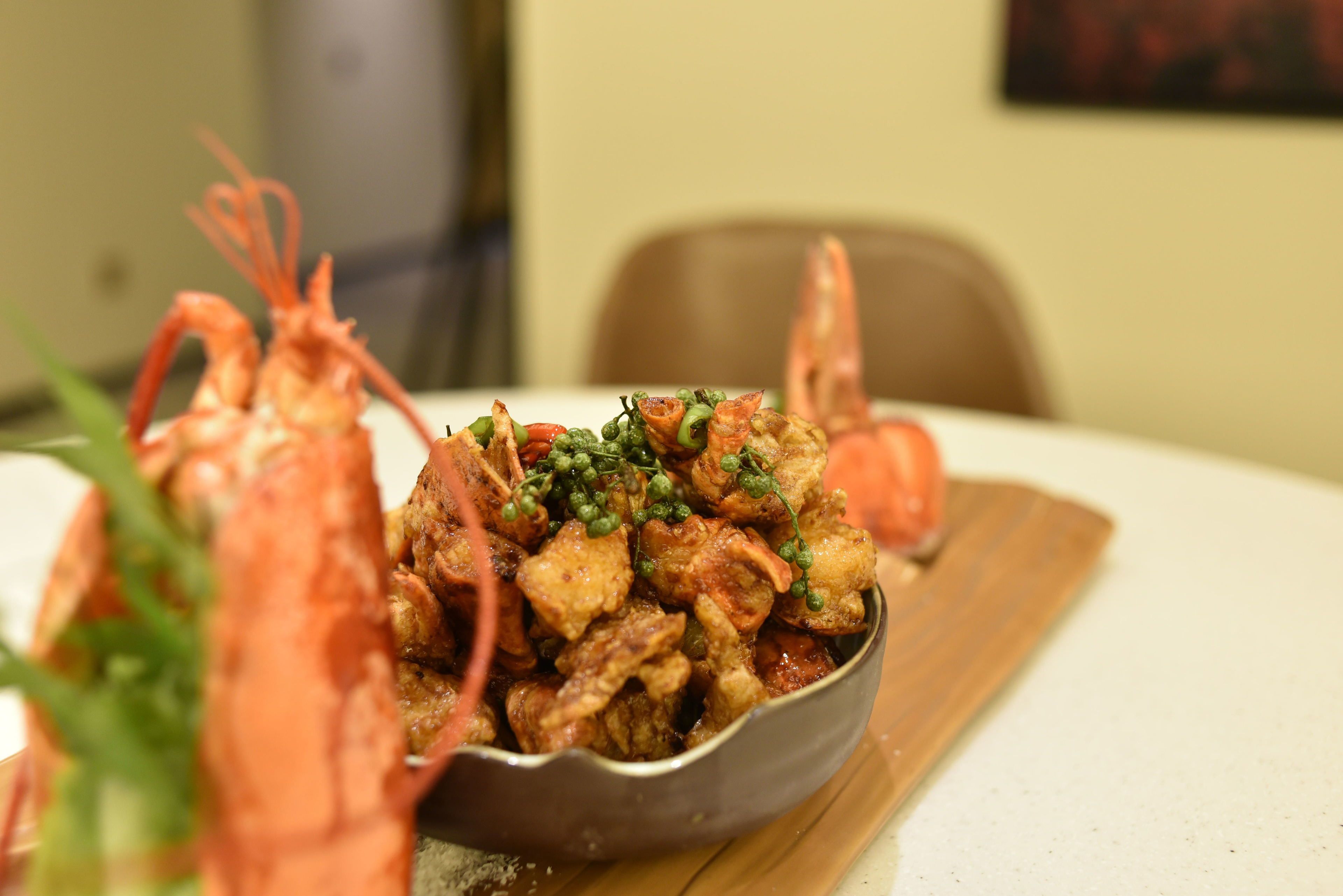A dining table with a bowl of food, including shrimp and vegetables.