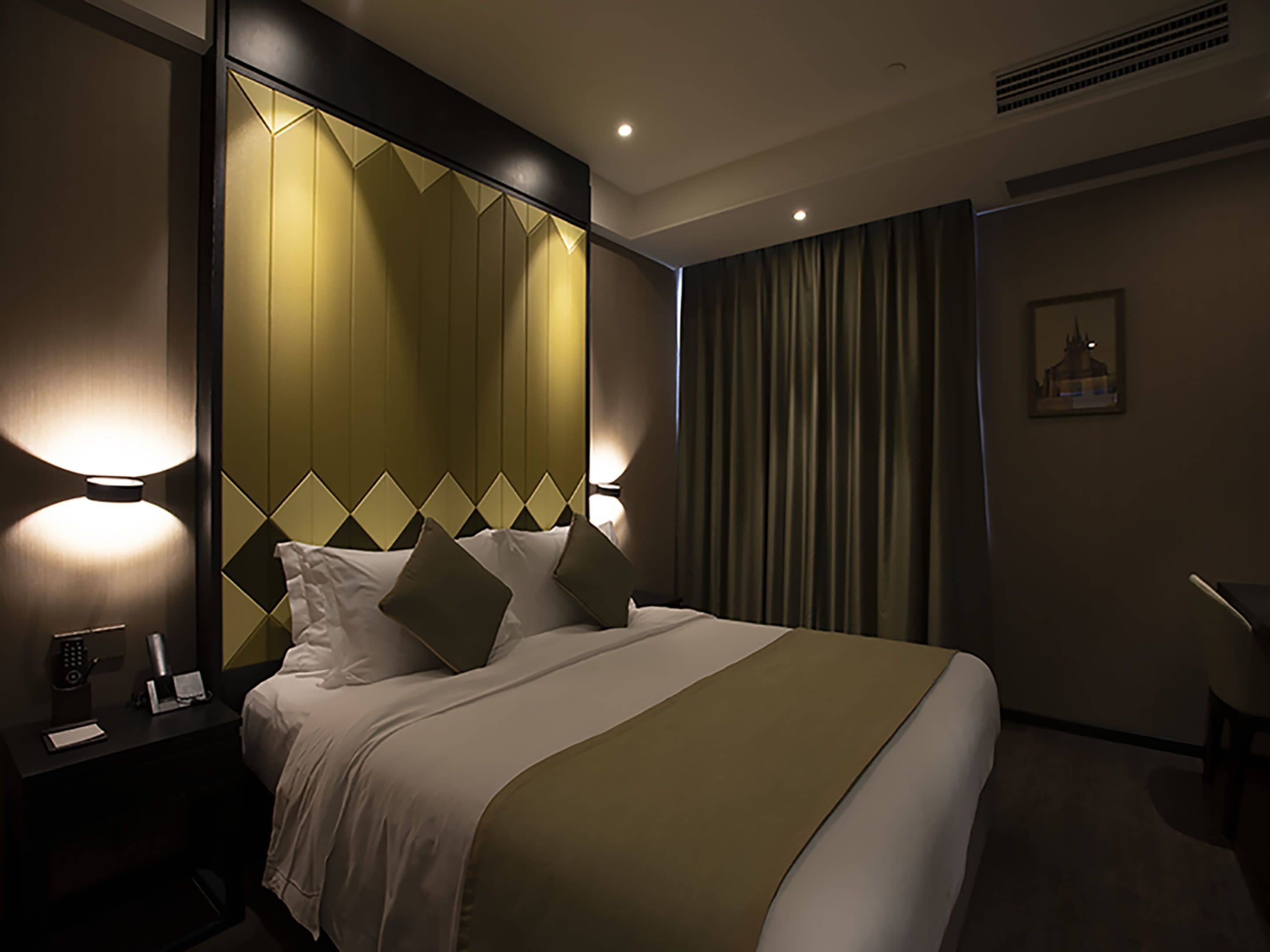 A hotel room with a large bed, bedside lamps, a nightstand, and a window with curtains.
