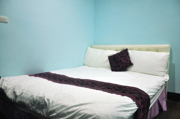 Una cama bien hecha con edredón blanco, una manta morada y una sola almohada decorativa.