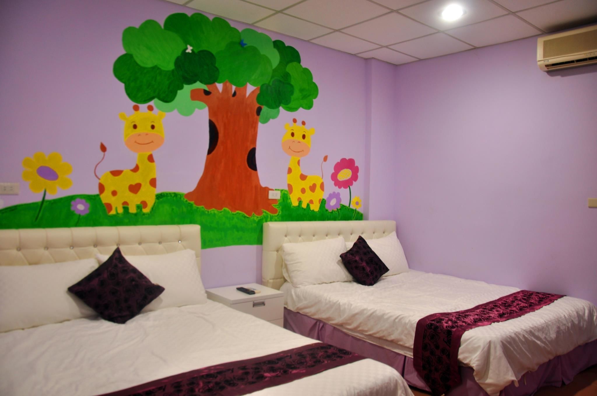 A room with two beds, a mural of giraffes and a tree, and a purple wall.