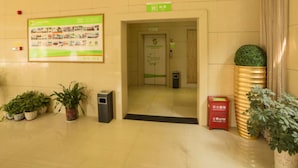 Un vestíbulo de hotel con mostrador de recepción, un letrero verde sobre la puerta y plantas en macetas.