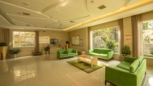 Un vestíbulo amplio con sofás verdes, una mesa de centro y una televisión.