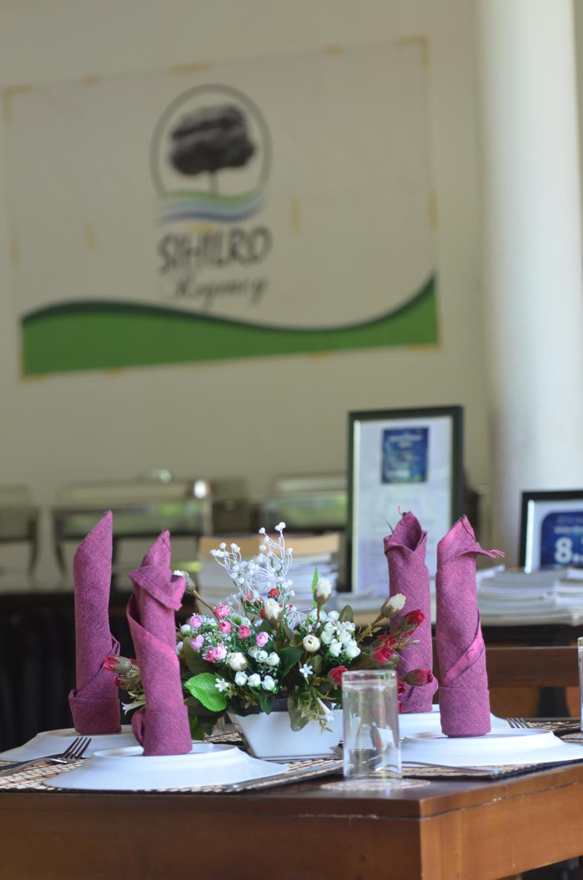 A neatly set dining table with a floral centerpiece, a framed picture, and a menu stand.