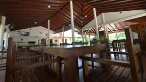 A spacious indoor area with wooden benches and tables, a high ceiling with wooden beams, and a view of the outdoors. - Sihilro Regency (Udawalawa)