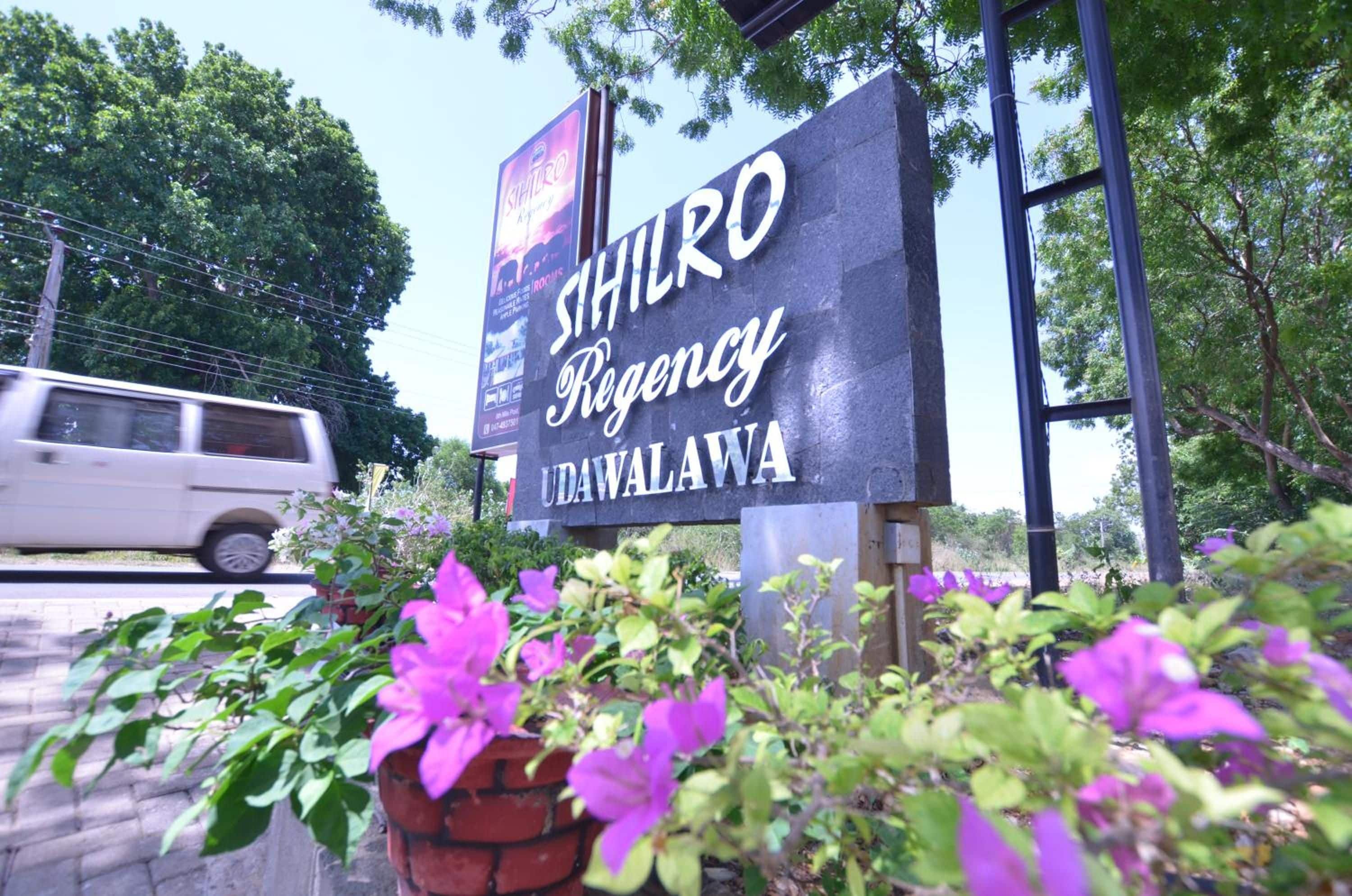 A sign for a hotel named 'SIHILRO Regency UDAWAWA' with a vehicle passing by in the background.