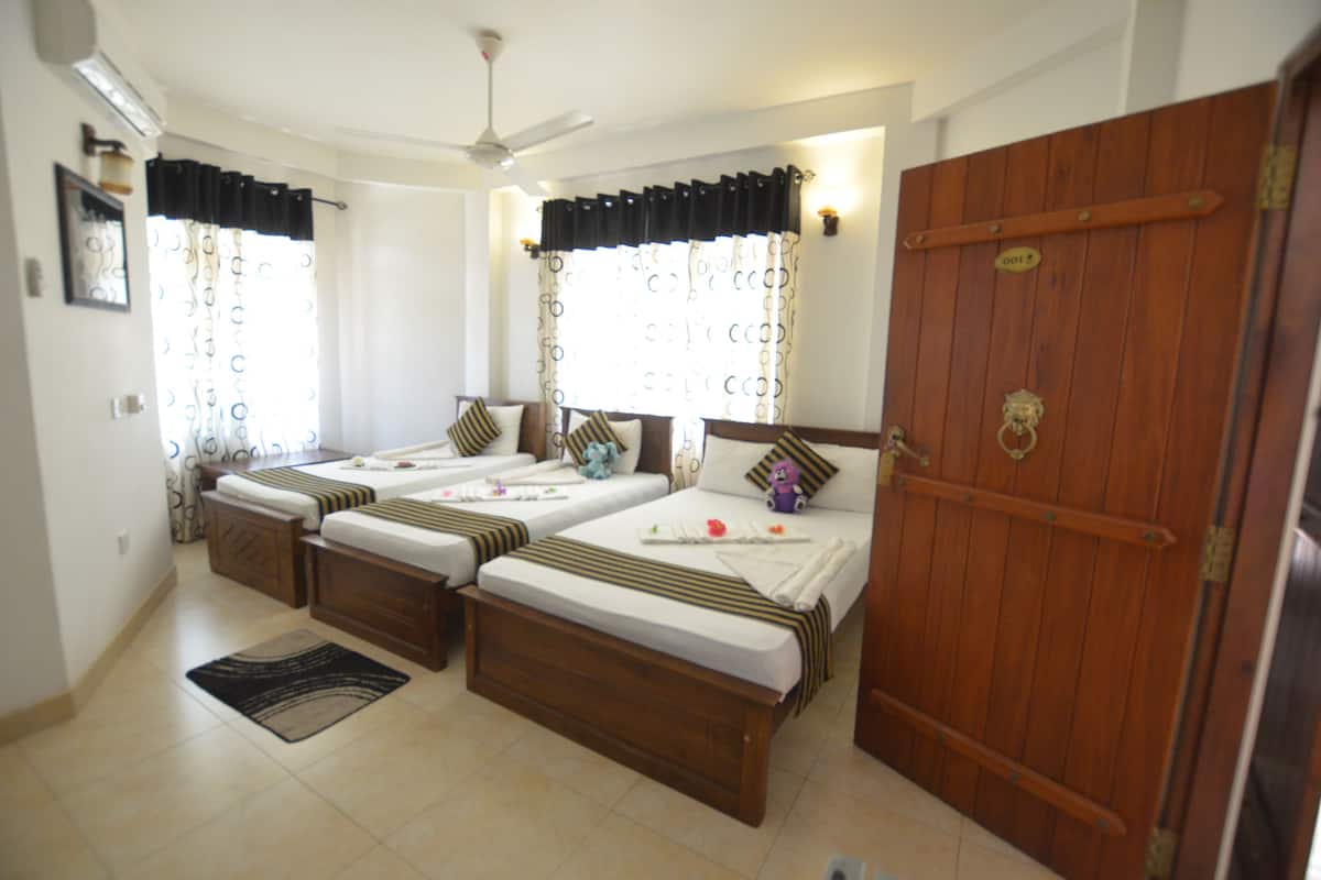 A room with three beds, a wooden door, and a ceiling fan.