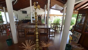 A spacious indoor area with wooden tables and chairs, a central decorative metal sculpture, and potted plants. - Sihilro Regency (Udawalawa)