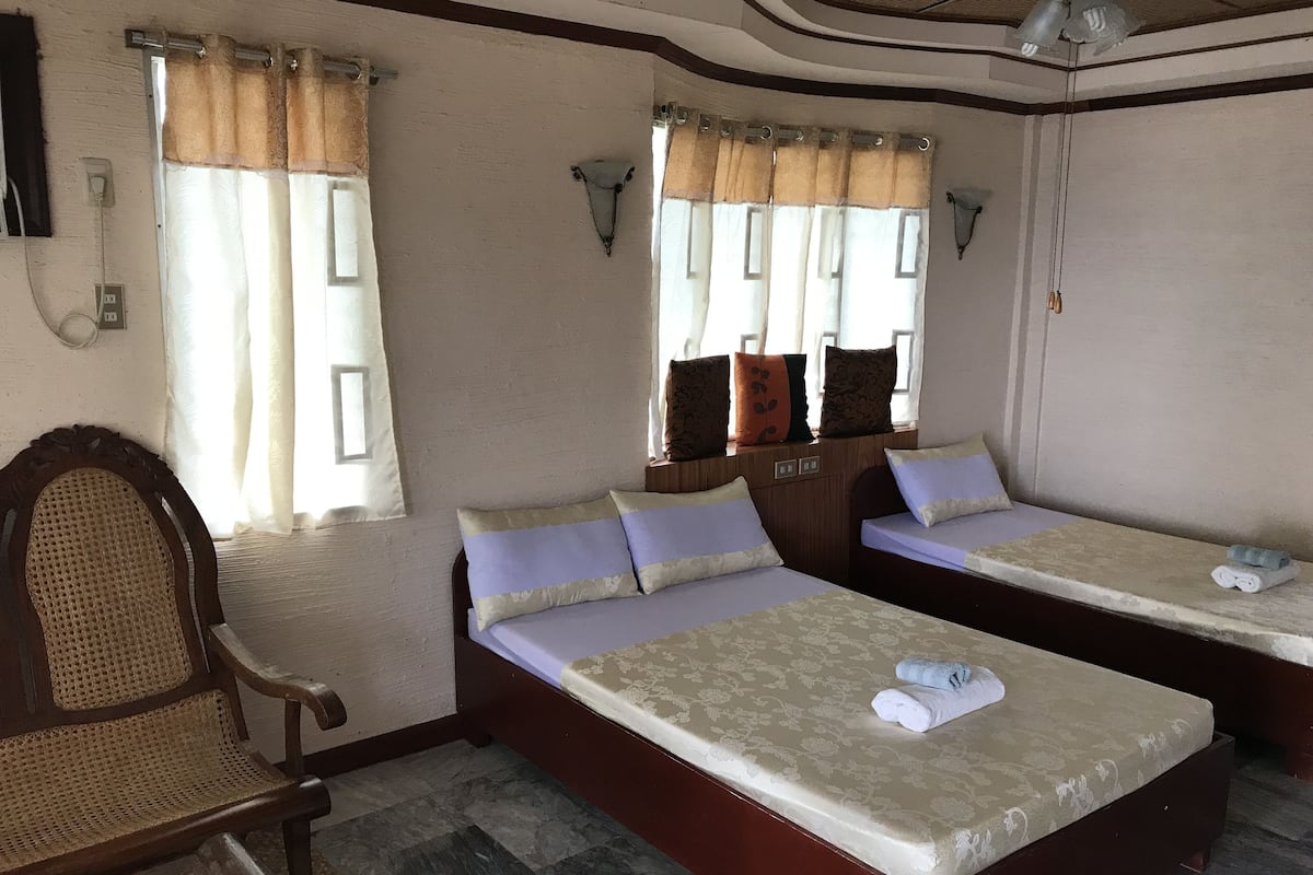 Habitación de hotel con dos camas, una silla de madera y una mesita con toallas.