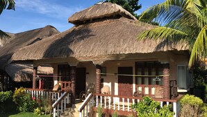 A traditional thatched-roof house with a porch, surrounded by tropical vegetation. - Nova Beach Resort (Panglao)