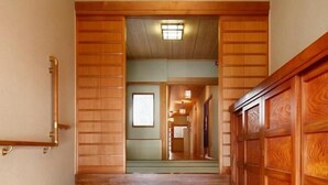 A hallway with wooden paneling and a tiled floor, leading to a room with a large window and a door. - Yadoya TENKU - Hostel (Asago)