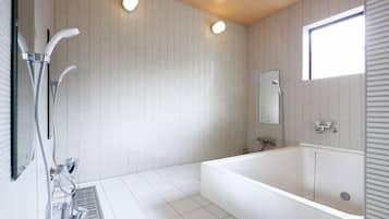 A modern bathroom with a large bathtub, a shower area with multiple faucets, and a window providing natural light.