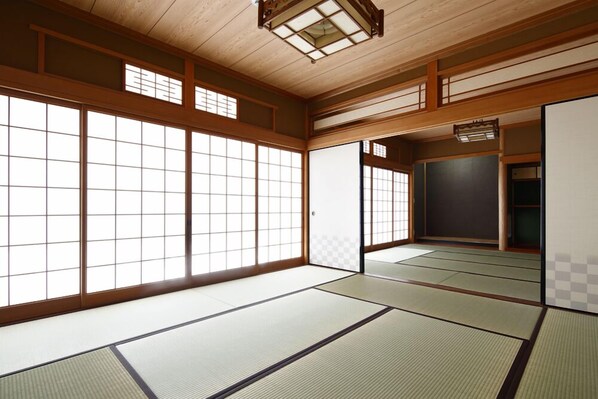 A traditional Japanese room with tatami flooring, sliding doors, and a shoji screen. - Yadoya TENKU - Hostel (Asago)