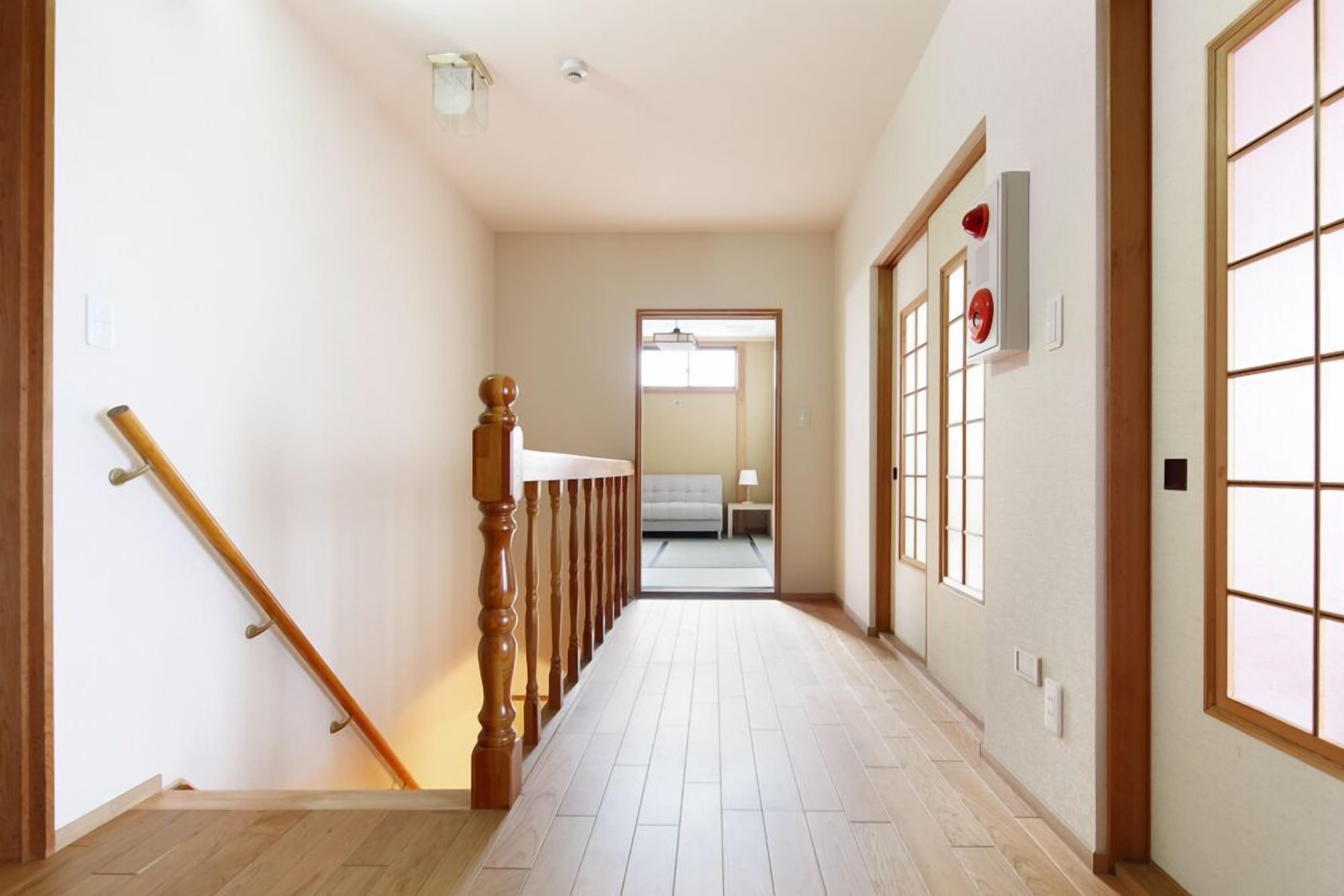A hallway with a wooden staircase, a light-colored floor, and a view into a room with a bed and a nightstand.