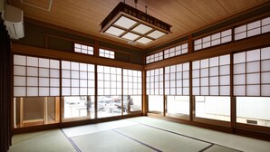 A traditional Japanese room with tatami flooring, sliding shoji doors, and a ceiling fan. - Yadoya TENKU - Hostel (Asago)