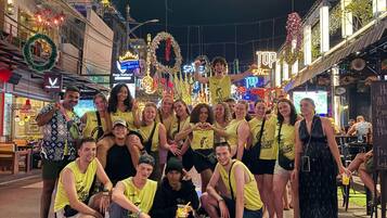 A group of people posing in front of a neon sign that reads 'PUB STREET' with various shops and decorations in the background.