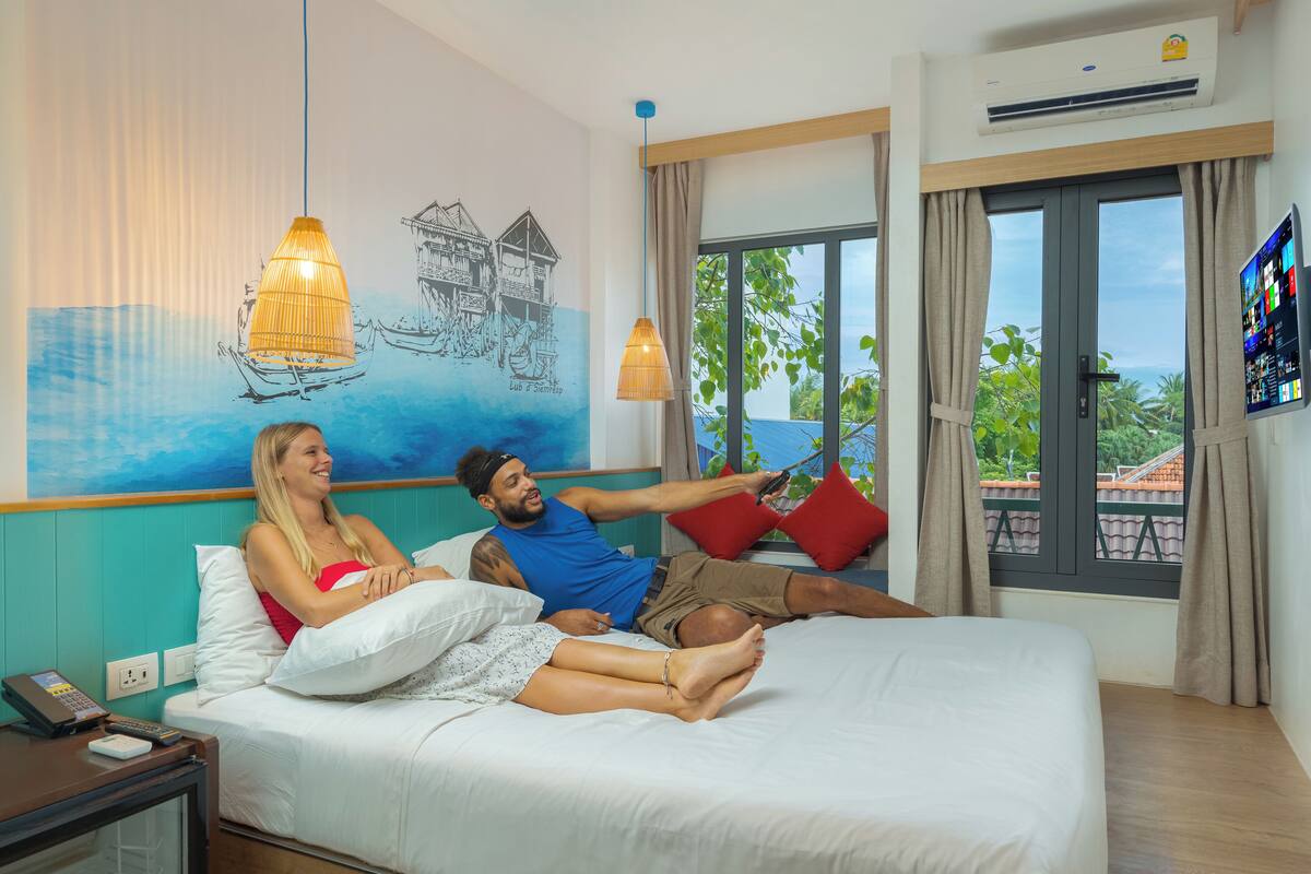 Ein Hotelzimmer mit einem Bett, einem Fernseher, einem Fenster mit Vorhängen und einer Wand mit Wandgemälde.