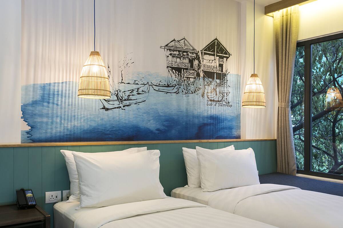 Ein Hotelzimmer mit zwei Betten, einer großen Wandmalerei von Booten und Häusern sowie zwei Pendelleuchten.