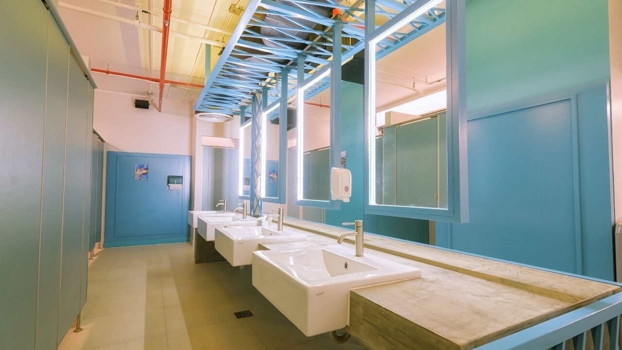 A row of sinks with mirrors, blue walls, and a tiled floor in a public restroom.