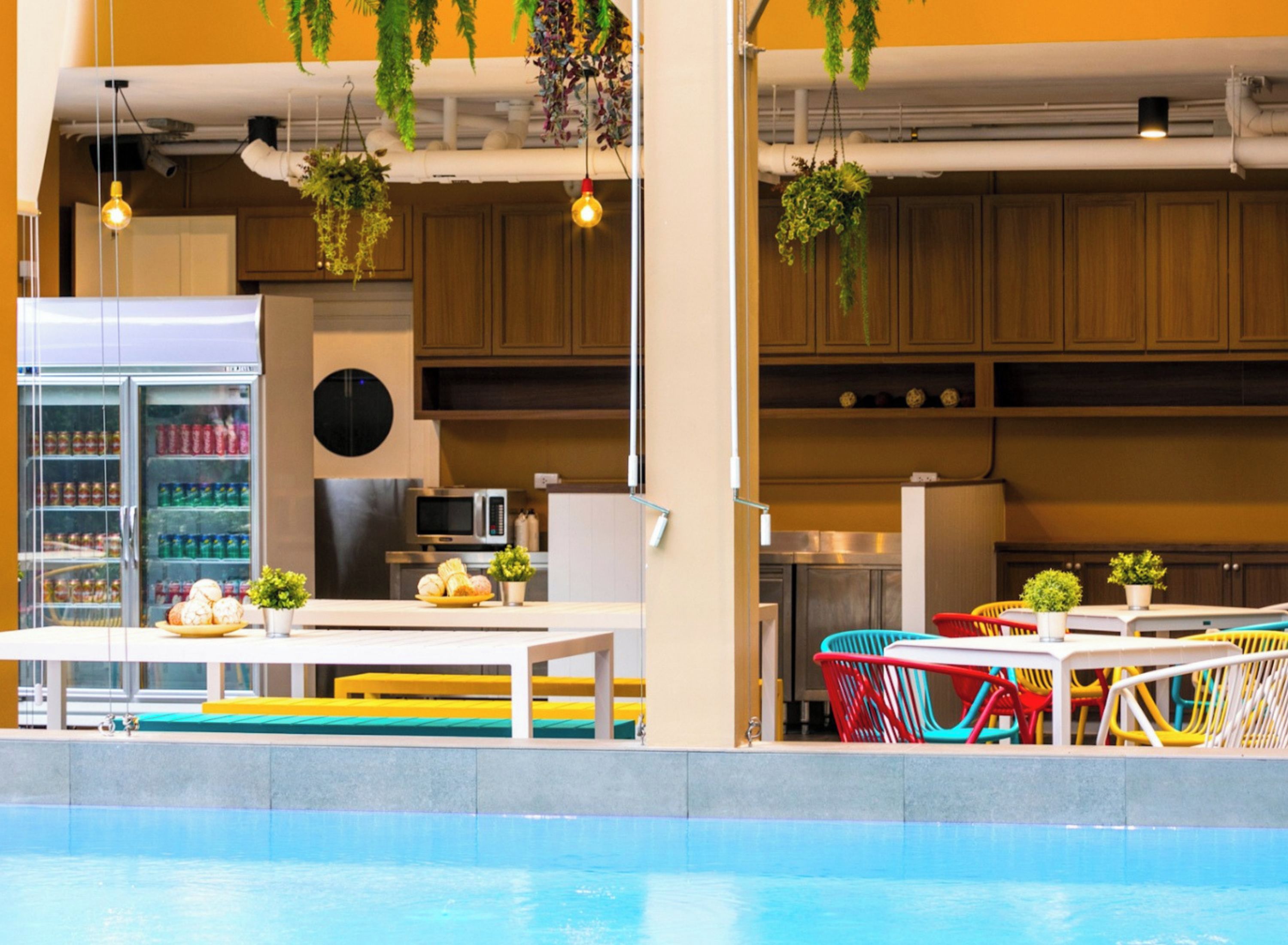 Un área junto a la piscina con mesa, sillas y un refrigerador lleno de bebidas.
