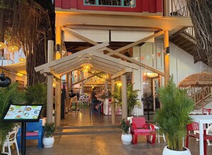 Ein Restaurant mit Innenbereich und überdachter Sitzgelegenheit, Tischen, Stühlen und Topfpflanzen.