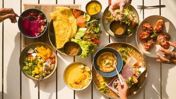 Una mesa con varios platos, entre ellos un tazón de sopa, un plato de verduras y un recipiente con fruta cortada.