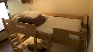 Una cama litera con estructura de madera, ropa de cama blanca y una pequeña estantería encima.