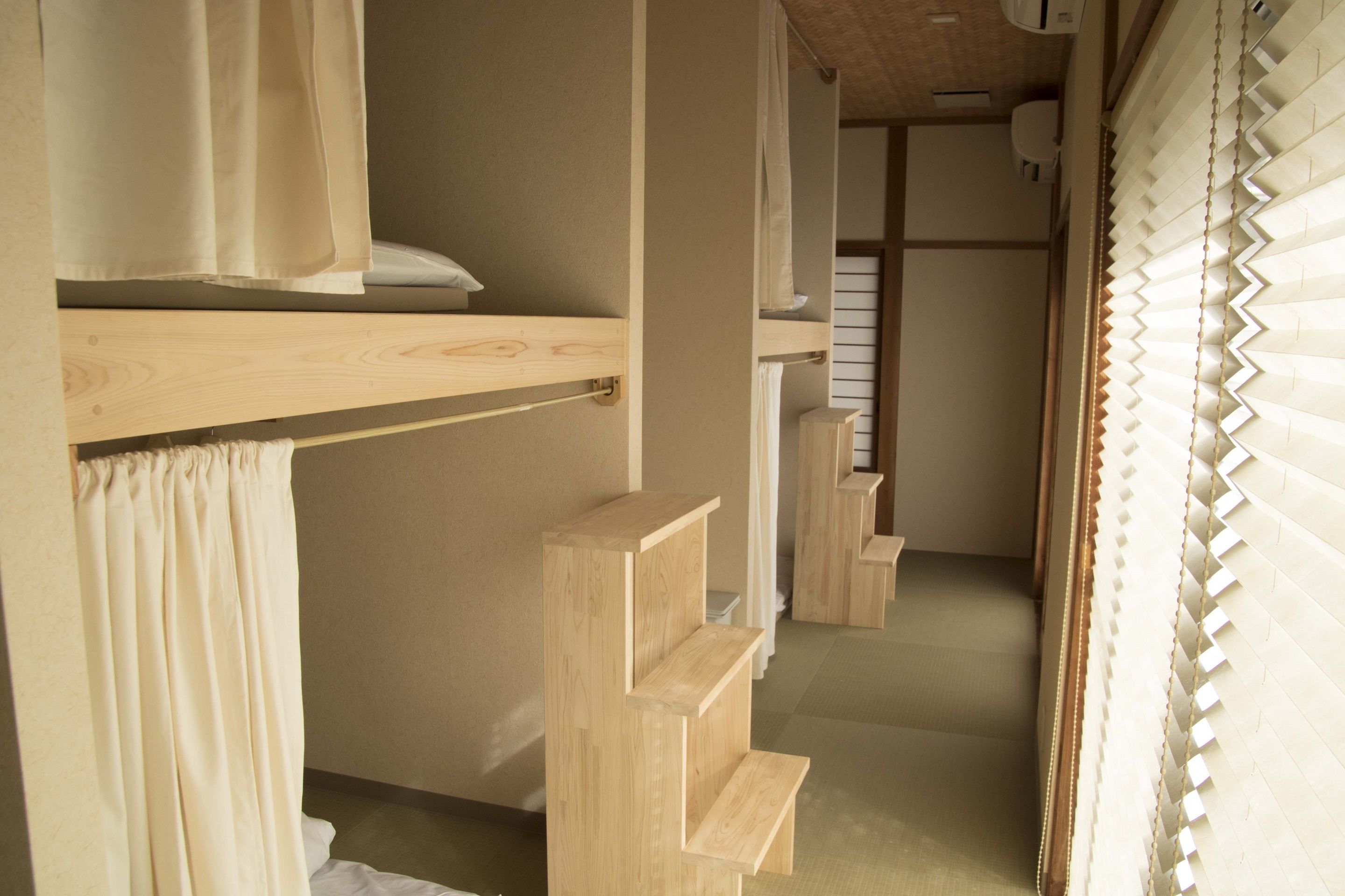 A room with a bunk bed, a wooden shelf unit, and a window with blinds.
