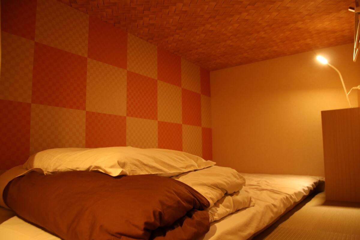 A single bed with white and brown bedding, a brick-patterned wall, and a bedside lamp.