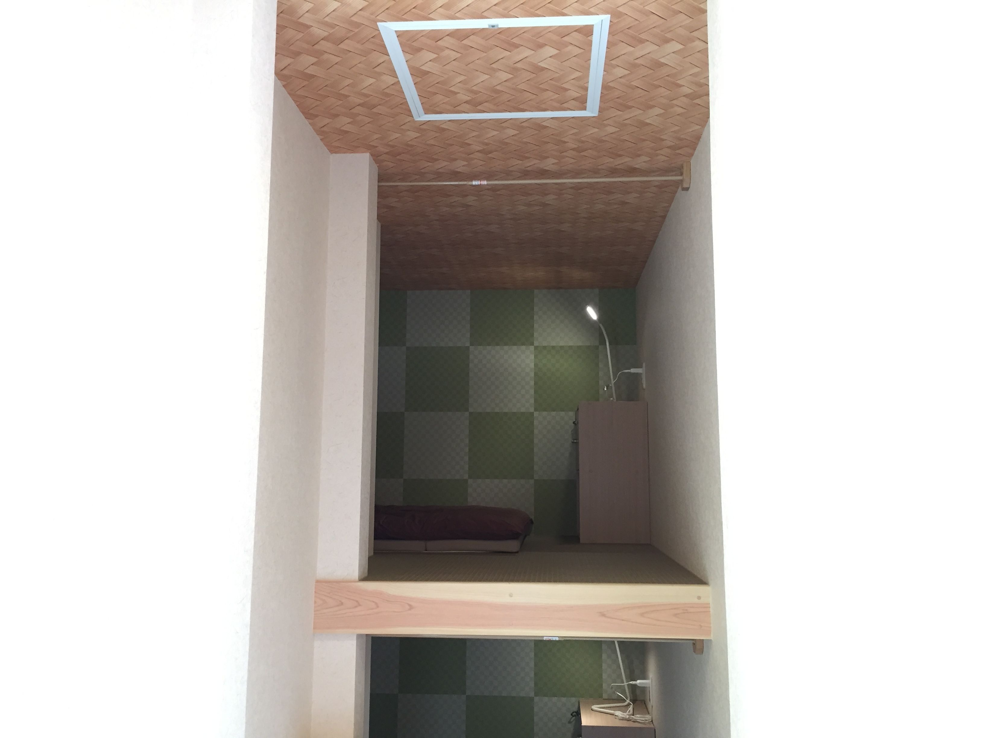 Une petite pièce aux dimensions réduites, avec un plafond en pente, un motif à carreaux sur un des murs, un lit simple et un espace bureau.