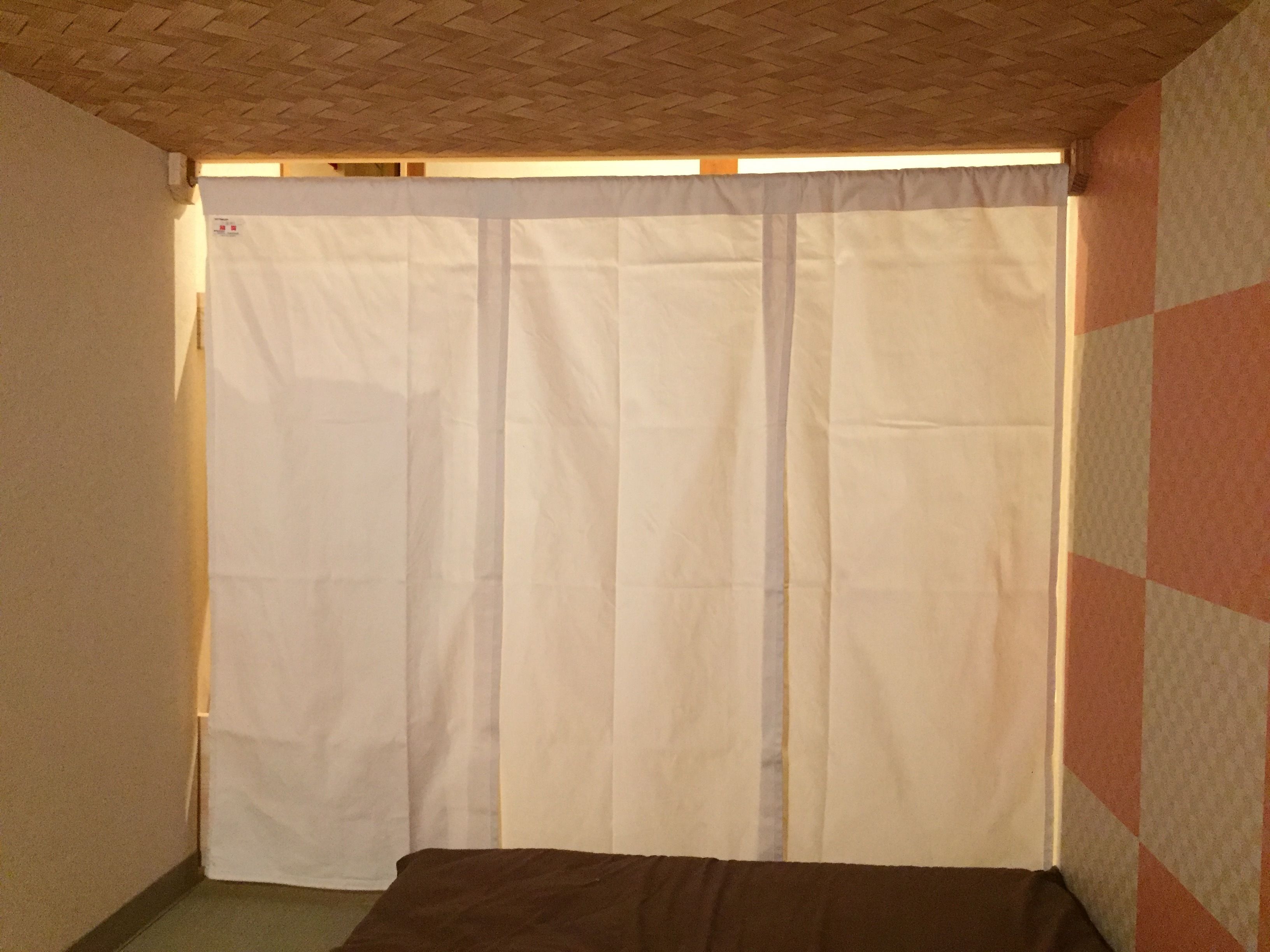 A room with a bed, a white curtain, and a patterned wall.