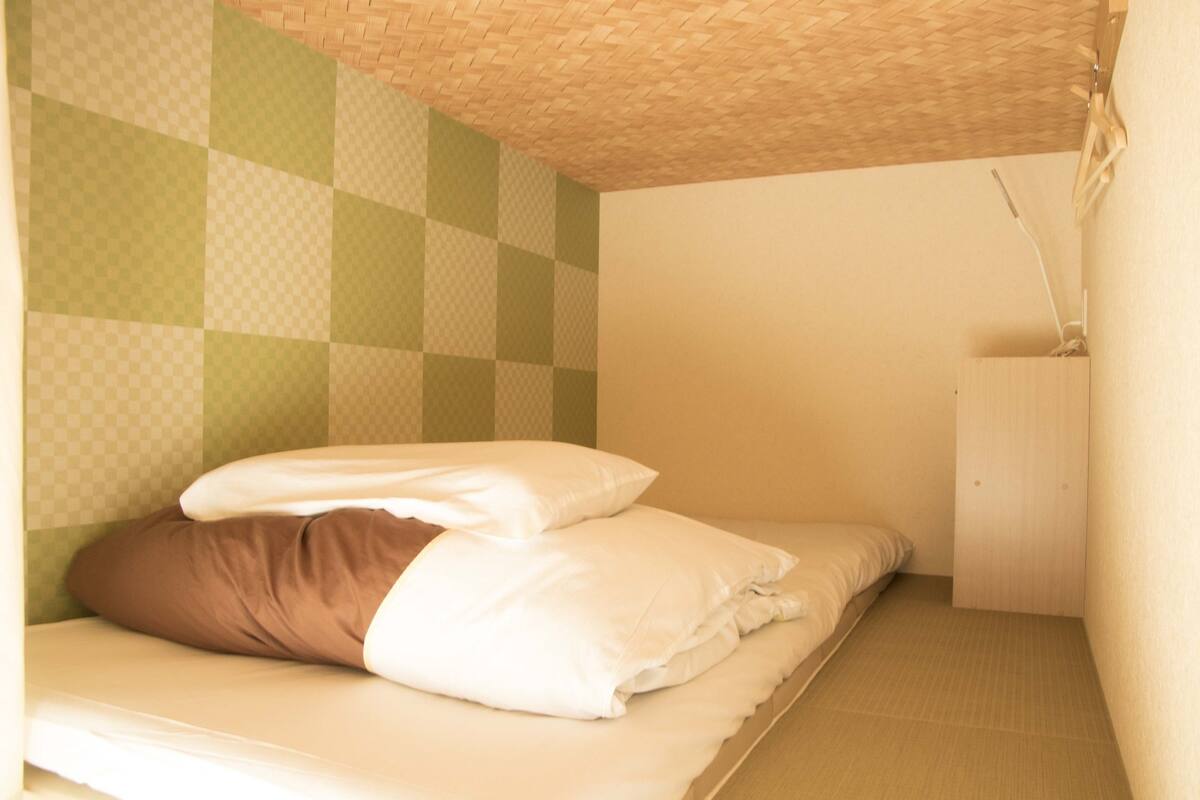 A single bed with white and brown bedding in a room with a checkered green and white wall pattern and a wooden ceiling.