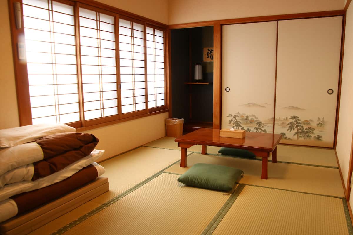 A traditional Japanese room with tatami flooring, a low wooden table, a green cushion, and a sliding shoji screen door.