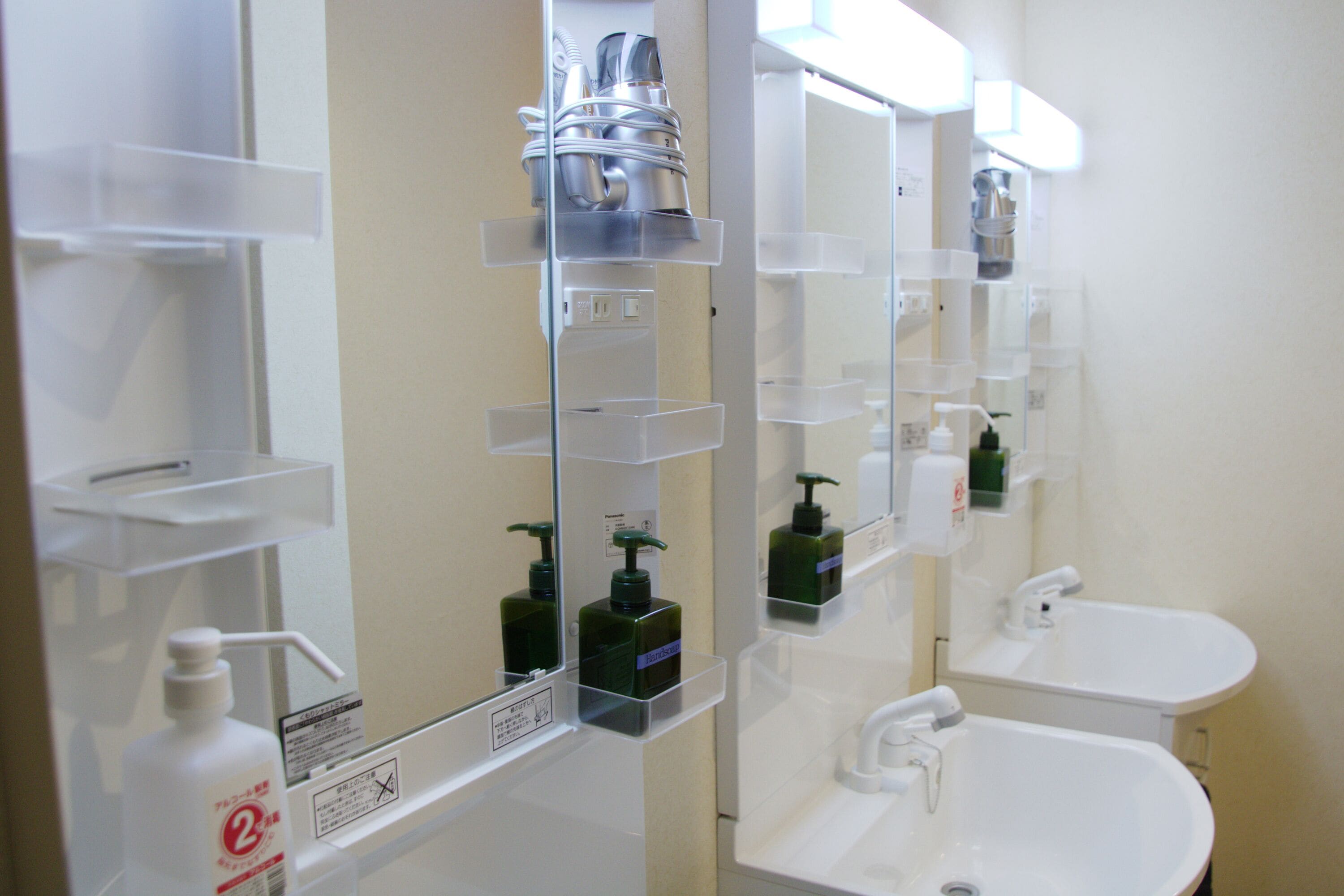 A bathroom with white sinks, a mirror, and shelves with toiletries.