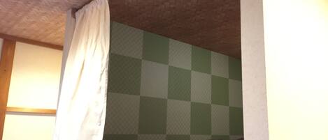 A room with a checkered wall, a bed with a brown mattress, and a white curtain.