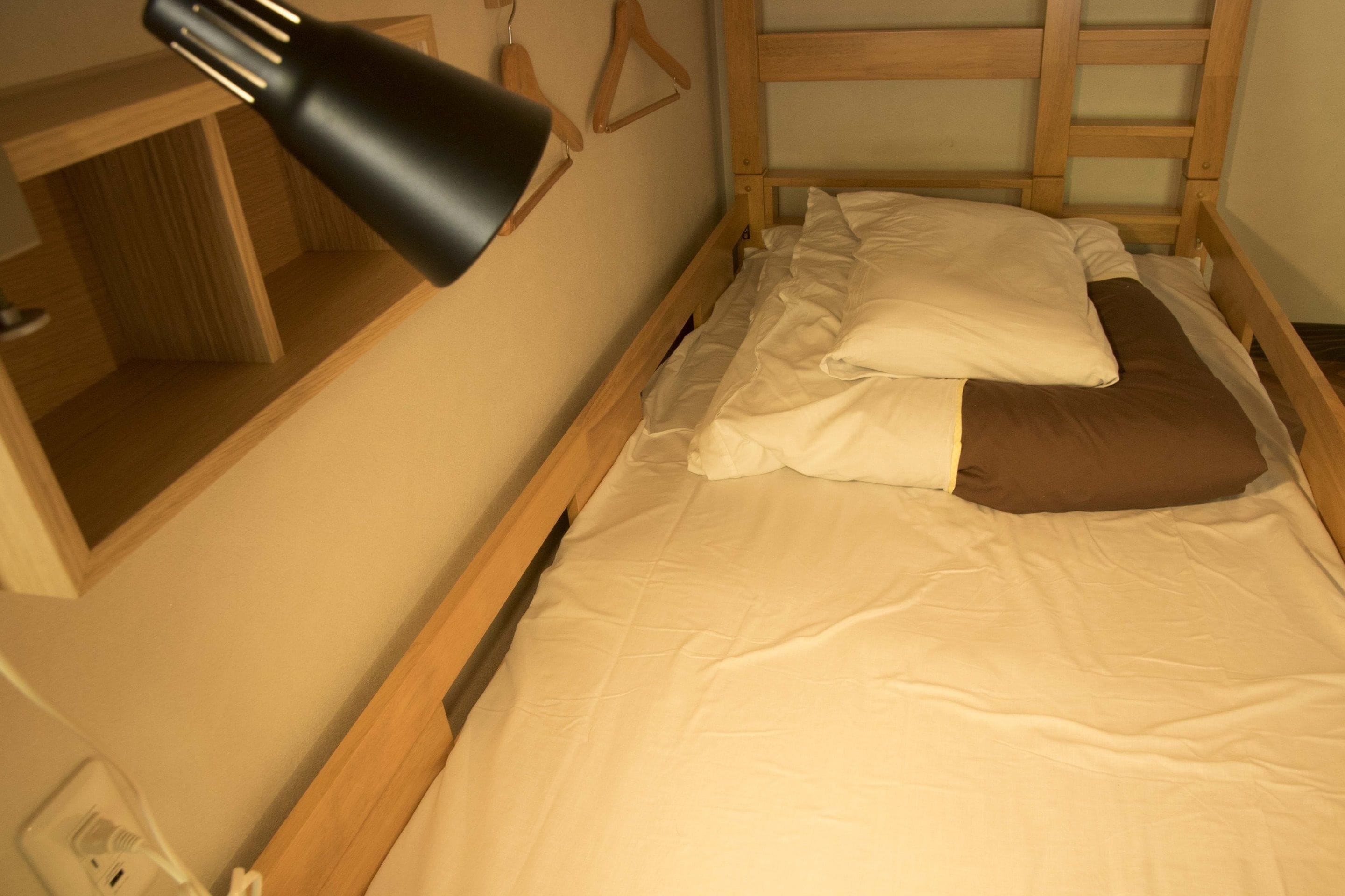 A single bed with a wooden frame, a bedside table, a lamp, and a wall-mounted hanger.