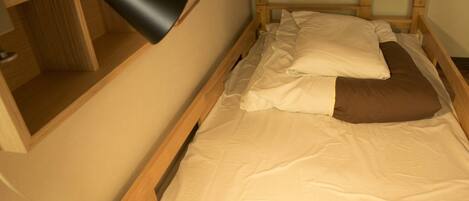 A single bed with a wooden frame, a bedside table, a lamp, and a wall-mounted hanger.