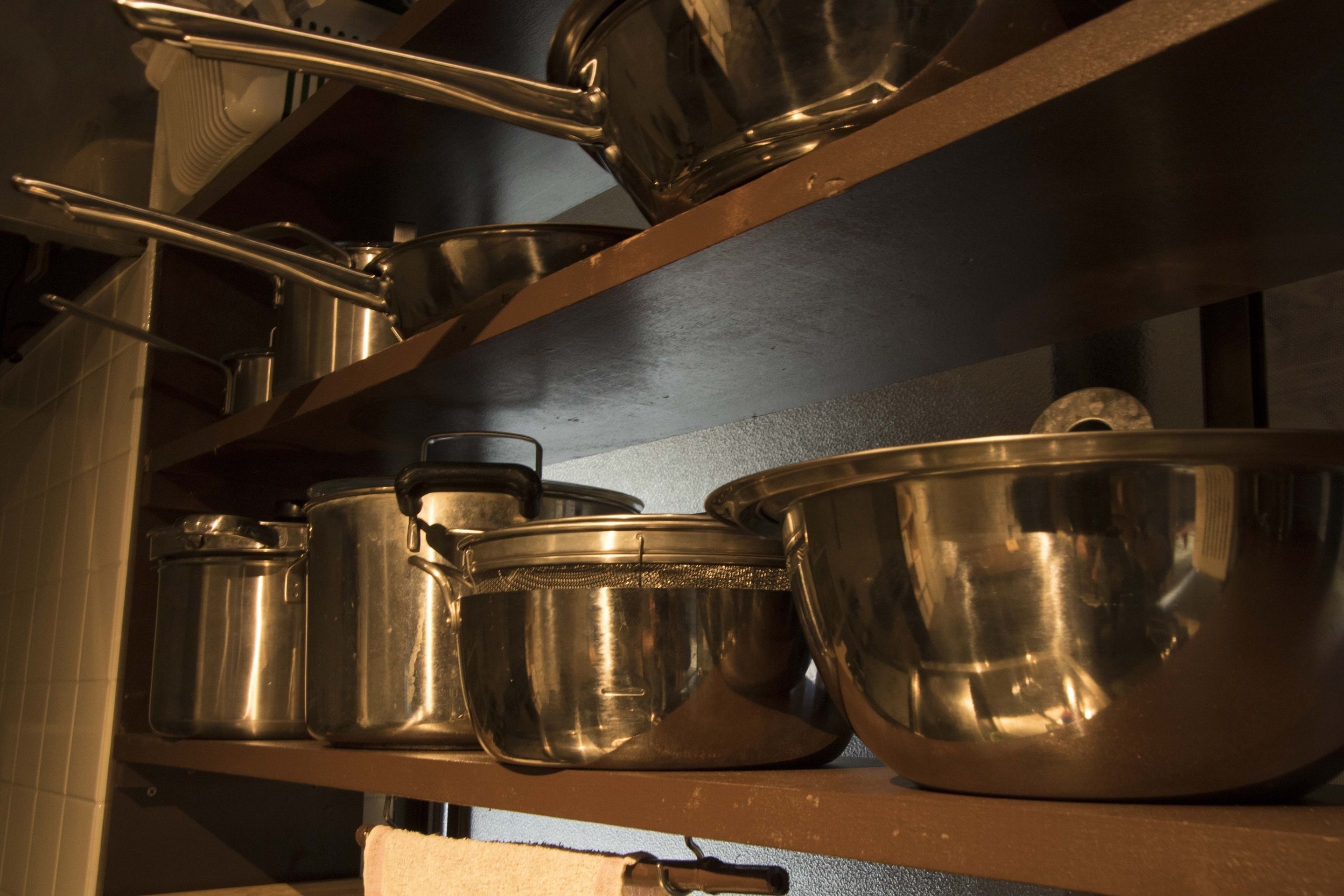 Uma prateleira na cozinha com utensílios de aço inoxidável, incluindo panelas, frigideiras e uma tigela grande para misturar.