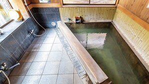 Een traditioneel Japans onsen met een houten interieur, een betegelde vloer en een klein houten plankje met toiletartikelen.