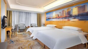 A hotel room with two beds, a cityscape painting, a desk, and a chair. - Vienna International Hotel （Longgang Universiade Center Subway Station） (Shenzhen)
