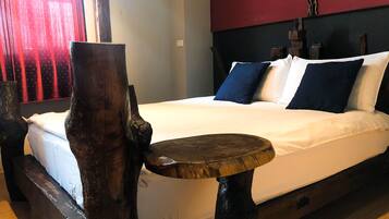 Uma cama com roupa branca, uma mesa de madeira redonda e um galho decorativo.
