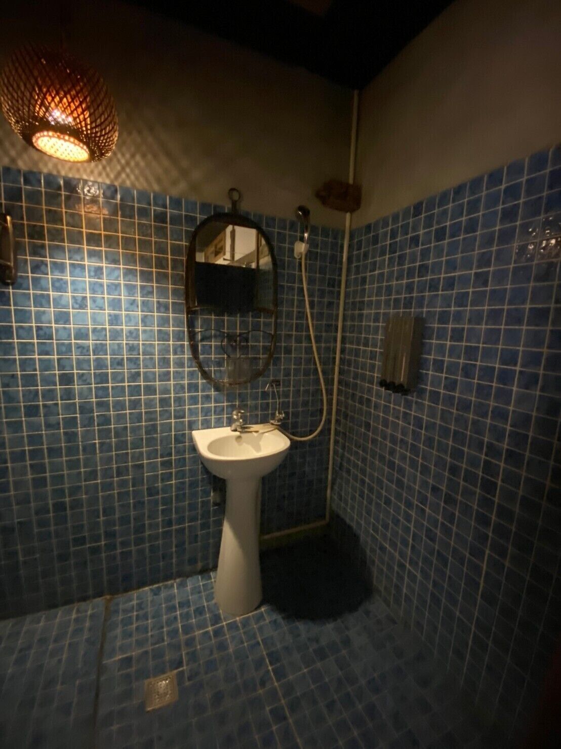 A bathroom with blue tiled walls, a white pedestal sink, a mirror, and a shower with a handheld showerhead.
