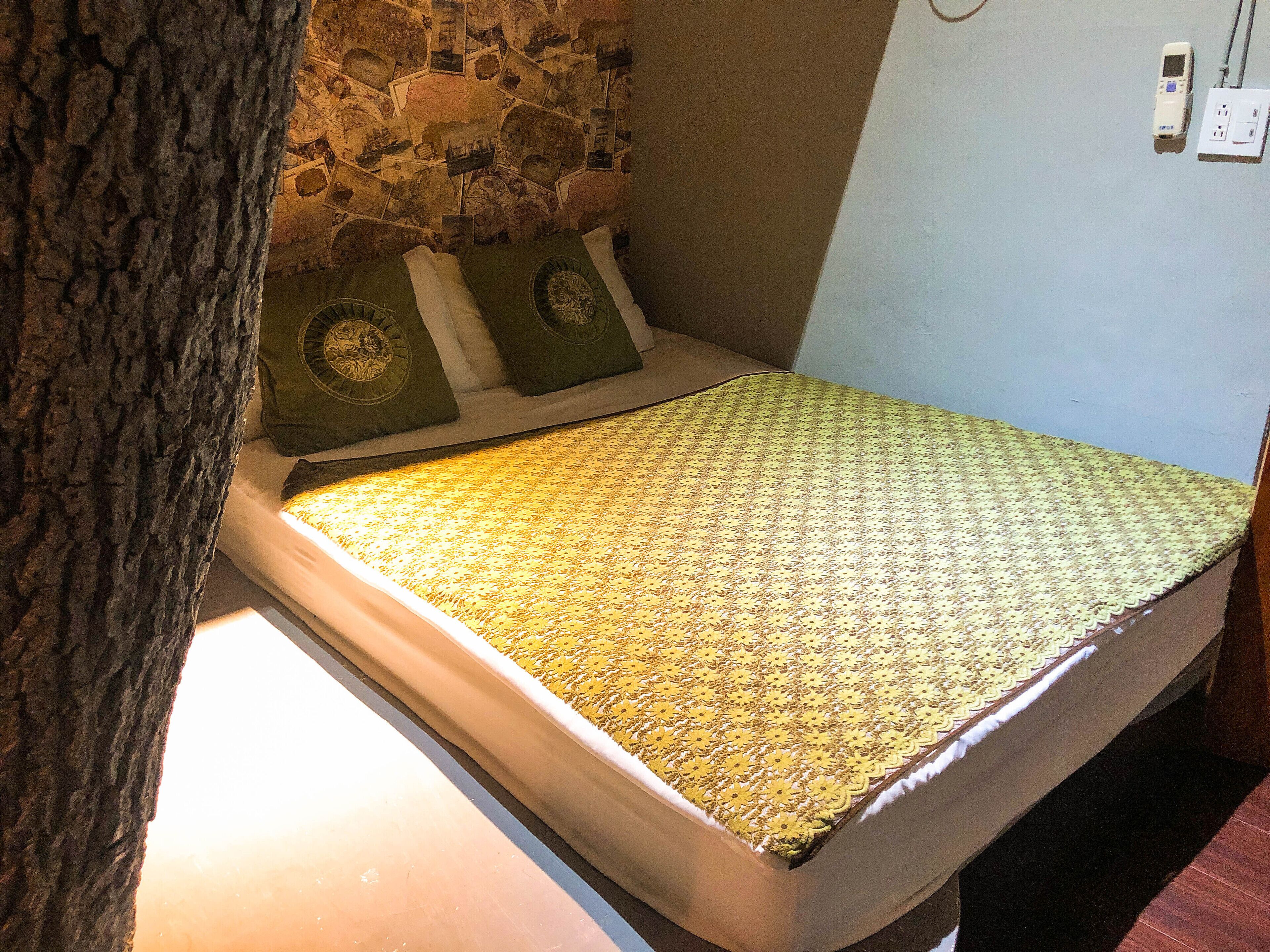 Un piccolo letto con una coperta a motivi, una parete in pietra sullo sfondo e una presa elettrica sulla parete.