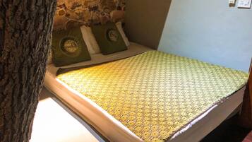 Un piccolo letto con una coperta a motivi, una parete in pietra sullo sfondo e una presa elettrica sulla parete.