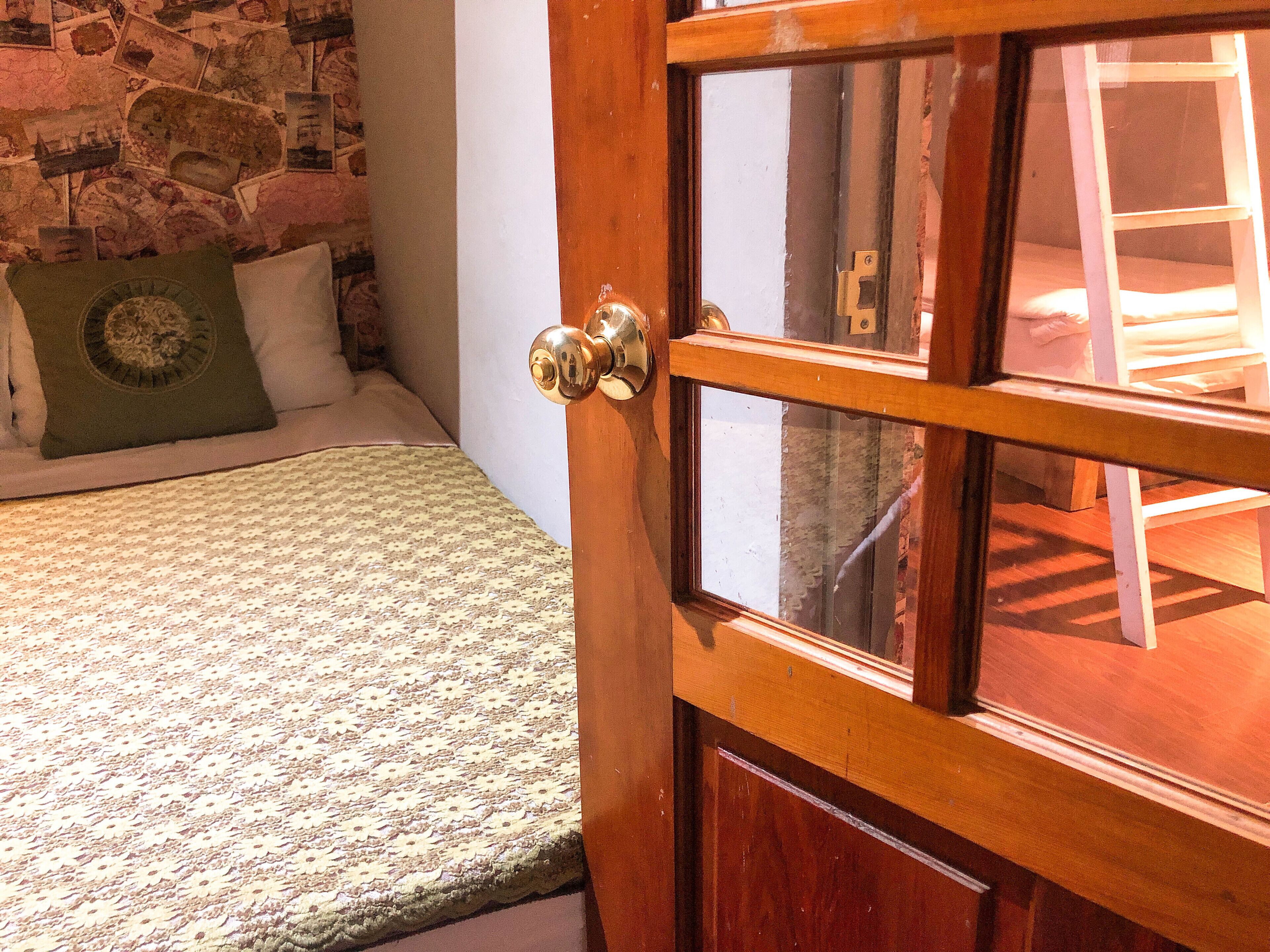 Uma porta de madeira com maçaneta de latão, uma parede de pedra e uma cama com roupa de cama estampada.