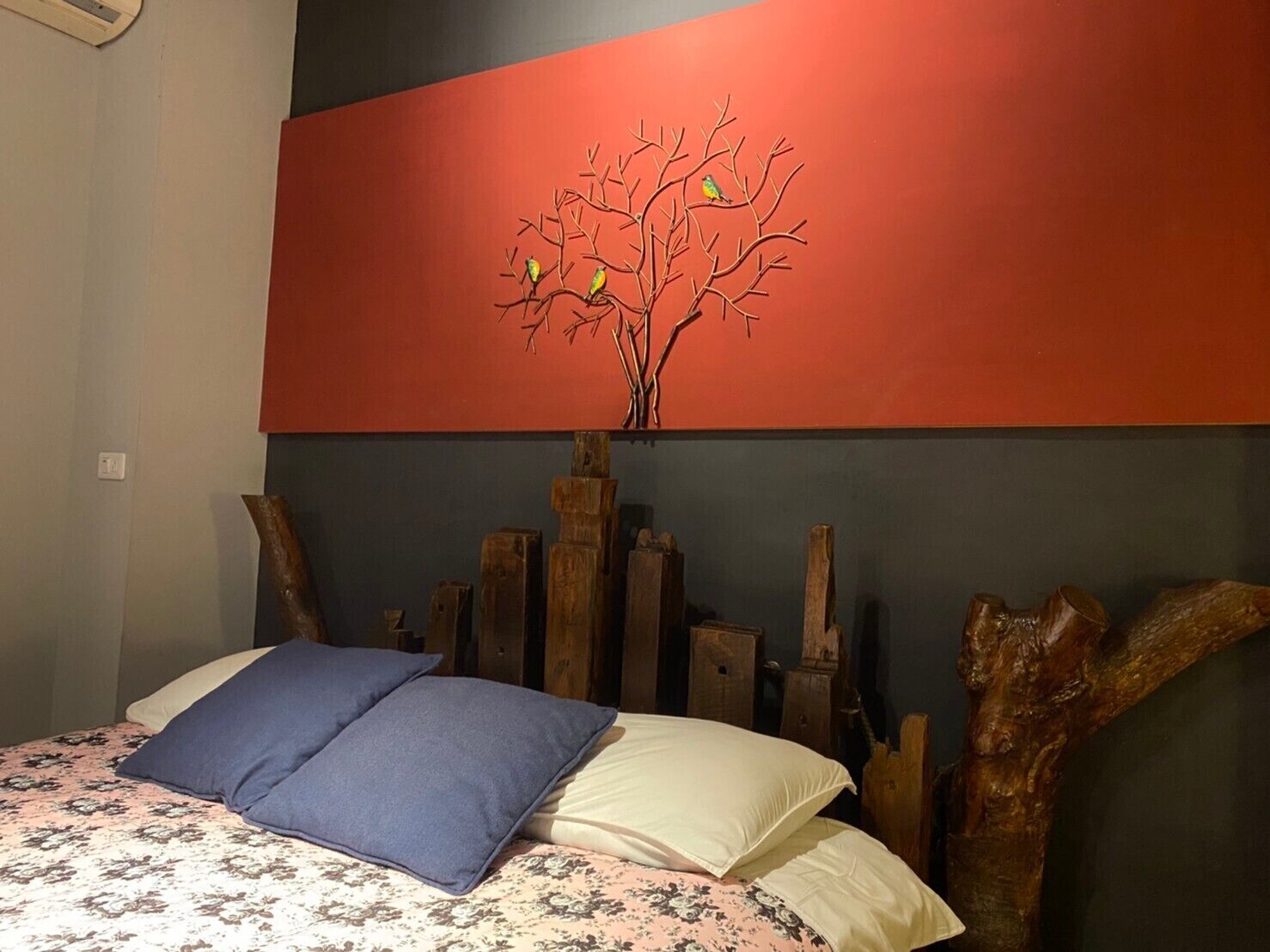 A bedroom with a bed, pillows, a wall-mounted painting of a tree, and wooden headboard.