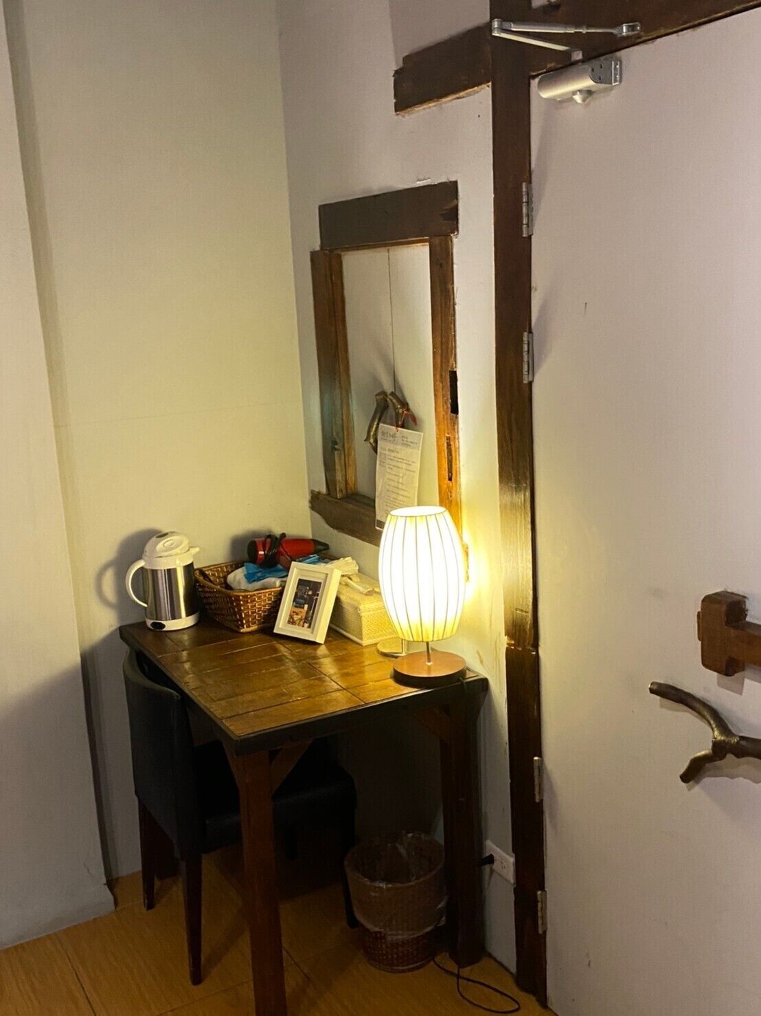 A small room with a wooden table, a lamp, a kettle, and a basket.