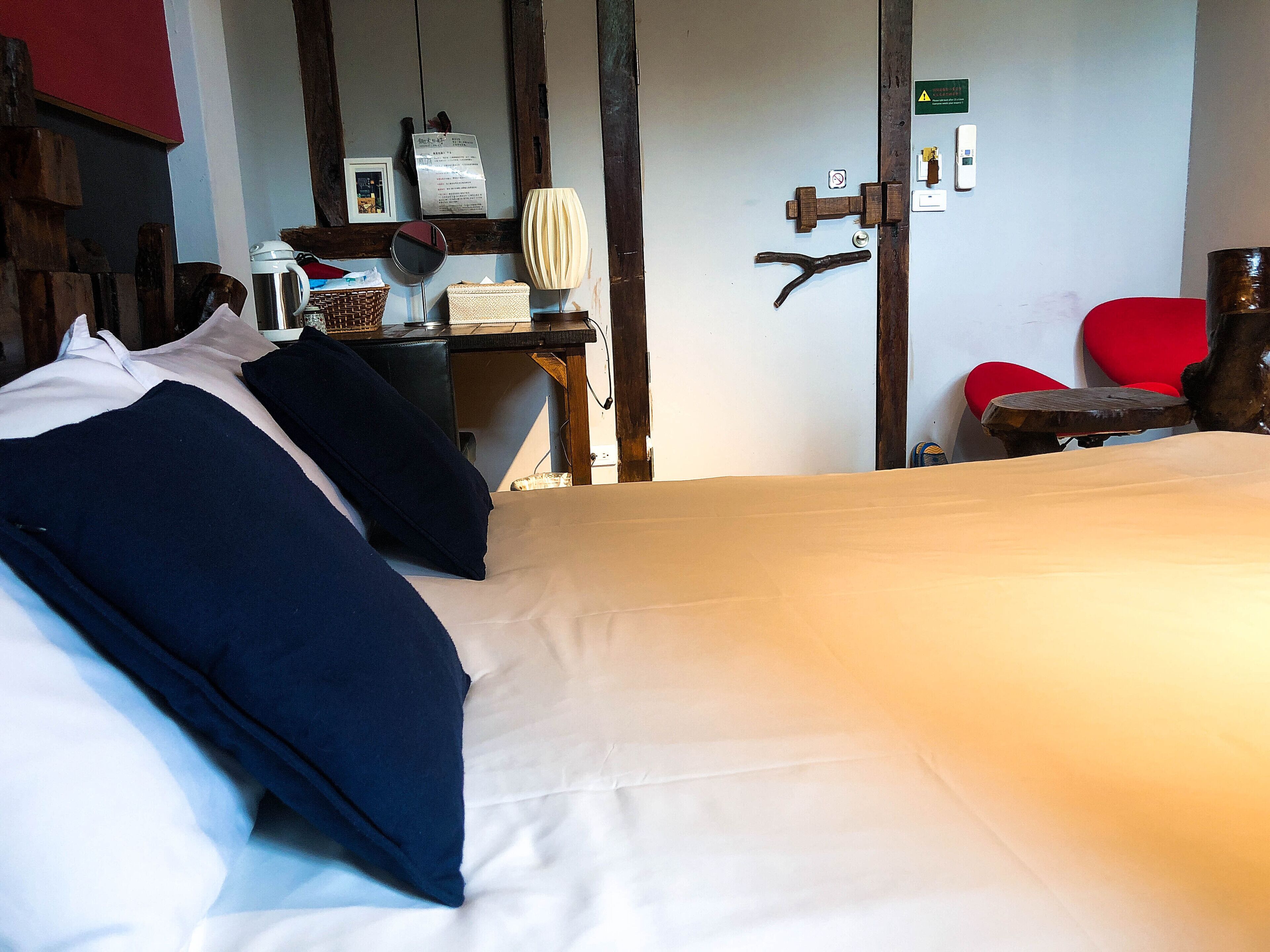 Un dormitorio con cama, almohadas, un escritorio con lámpara, una silla y una puerta con cerradura.