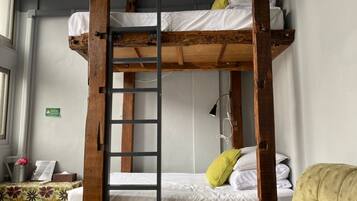 Una cama litera con escalera, ropa de cama blanca y una almohada verde.